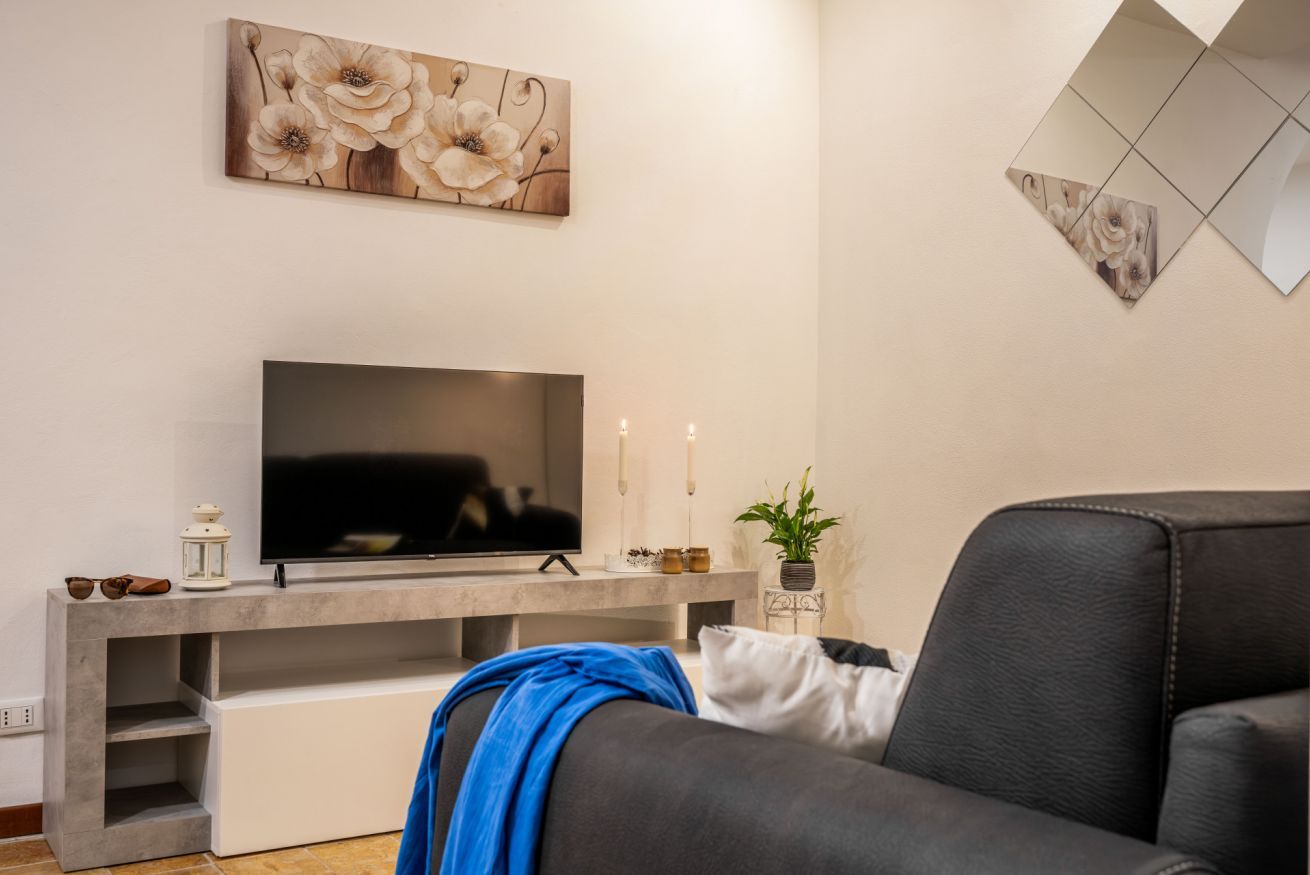Una sala moderna con una televisión de pantalla plana sobre una estantería empotrada, un sofá, arte decorativo en la pared y una planta en maceta.