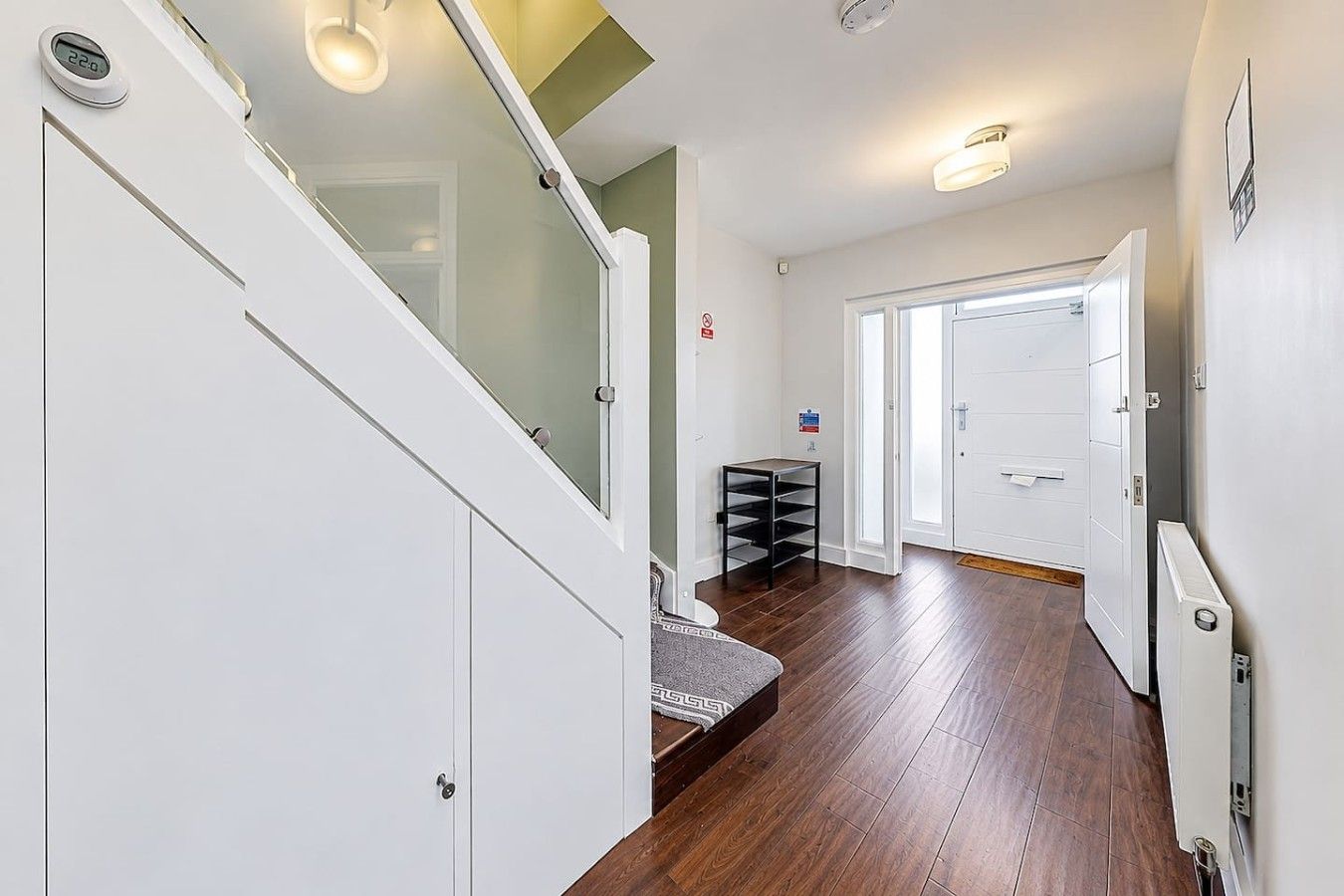 A hallway with a wooden floor, white walls, and a staircase with glass railings.