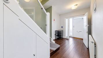 A hallway with a wooden floor, white walls, and a staircase with glass railings.