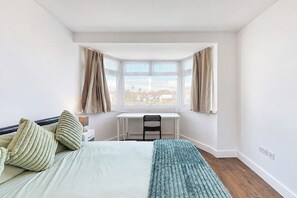 A bedroom with a bed, a desk, and a view through a bay window. - Wembley 3 Bath Home with Parking (Wembley)