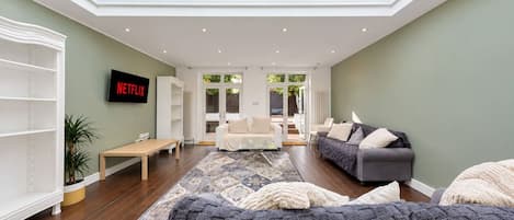 Una sala de estar moderna con techo alto, televisor de pantalla plana, sofá, mesa de centro y vista al exterior a través de una puerta de cristal.