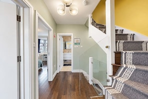 A hallway with a wooden floor, a glass railing staircase, and a door leading to another room. - Wembley 3 Bath Home with Parking (Wembley)