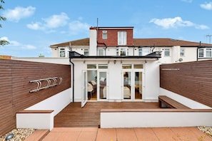 A two-story residential building with a covered patio area, a wooden fence, and a metal bike rack. - Wembley 3 Bath Home with Parking (Wembley)