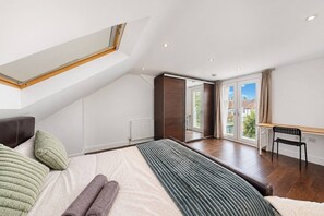 A bedroom with a skylight, a bed with pillows, a bench, and a view of the outside. - Wembley 3 Bath Home with Parking (Wembley)