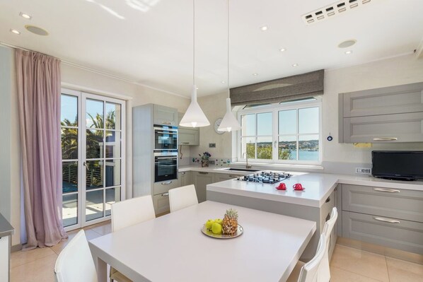 A modern kitchen with a dining area, large windows, and a view of the outdoors.