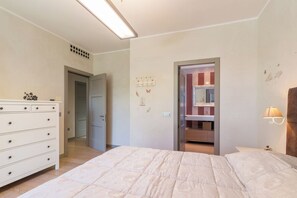 A bedroom with a bed, a dresser, a door leading to a bathroom, and a wall-mounted light fixture.