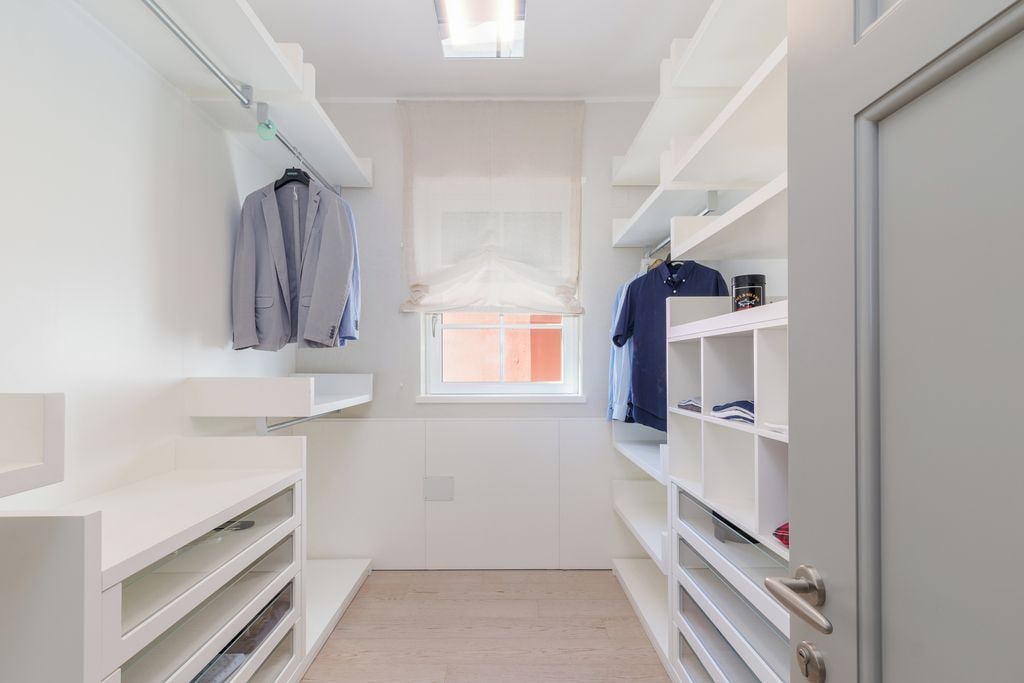 A walk-in closet with white shelving, a hanging rod, and a window.