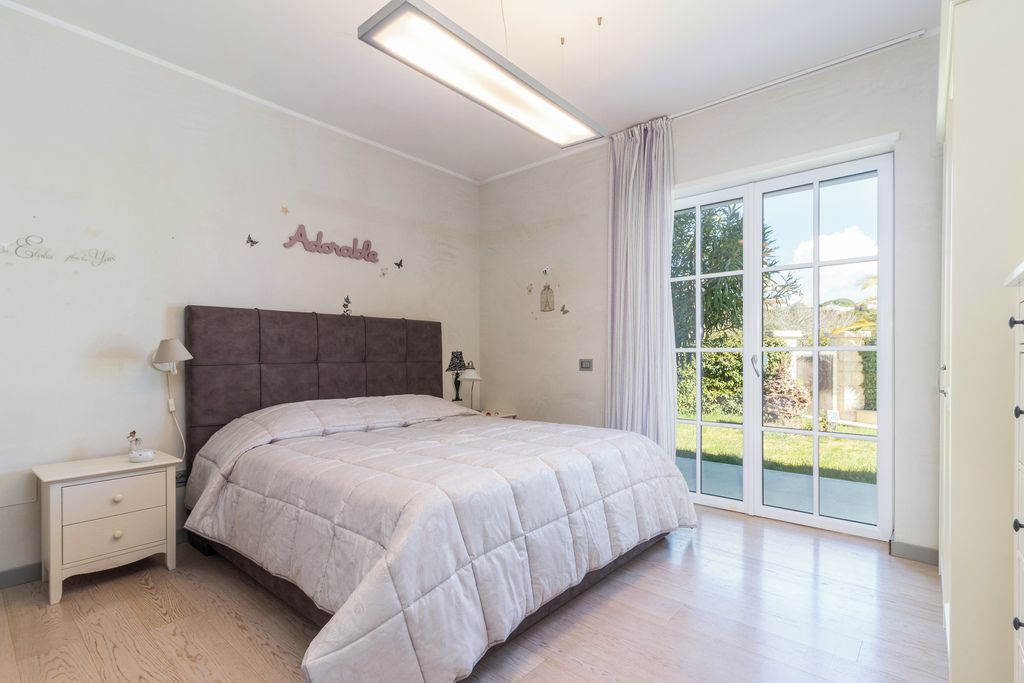 Ein Schlafzimmer mit Bett, Nachttisch, Lampe und Blick durch eine Glastür.