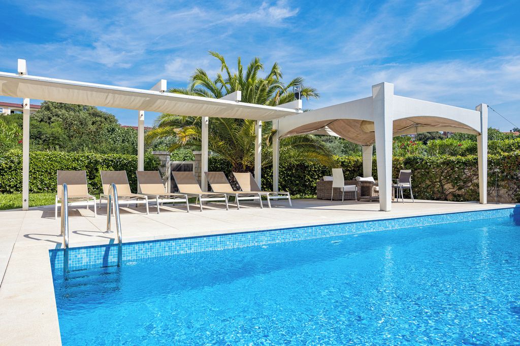 Piscina con sillas de descanso y sombrillas, rodeada de follaje.
