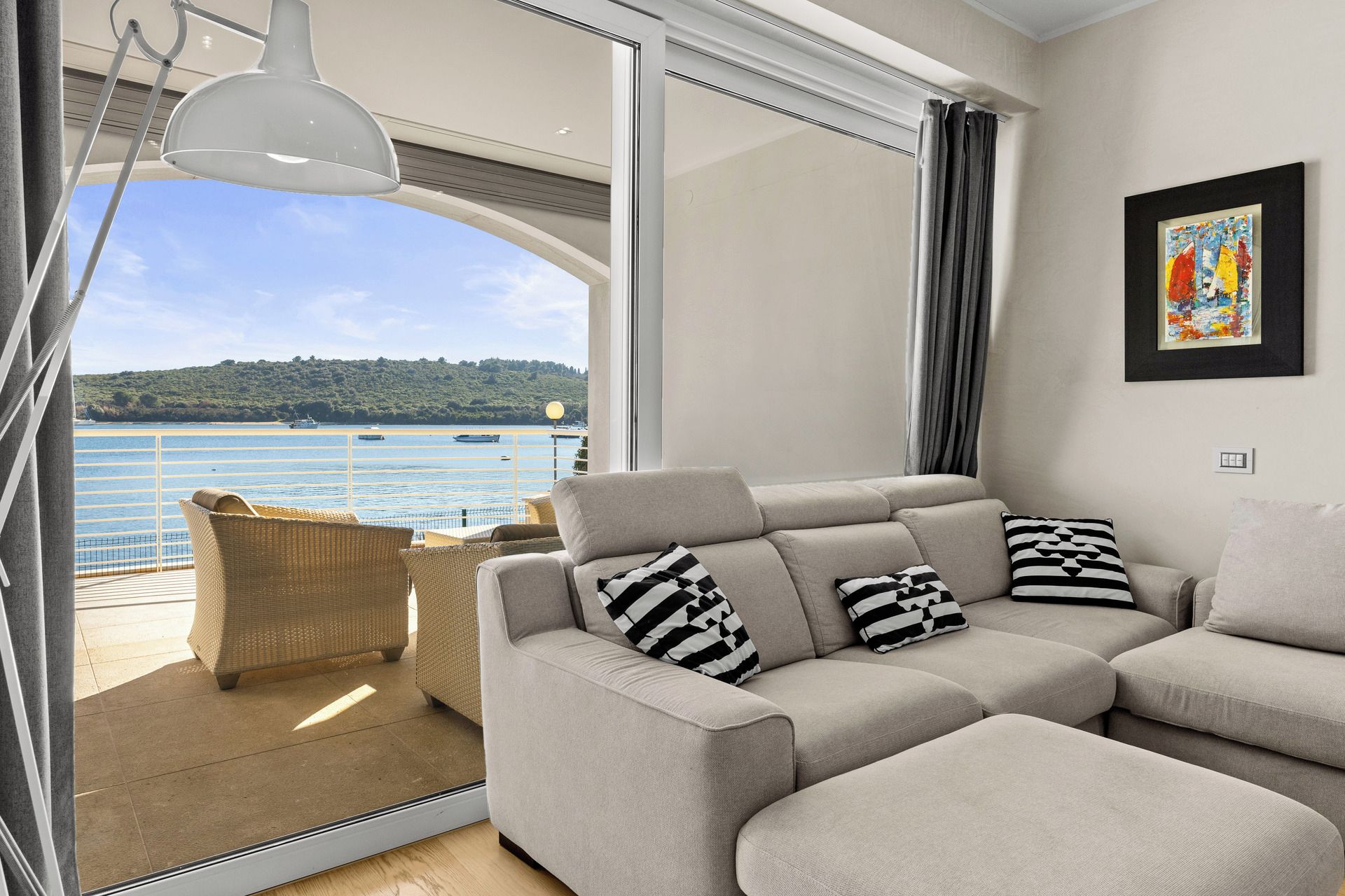 Una sala moderna con un sofá, cojines, una silla de mimbre y vistas al mar.
