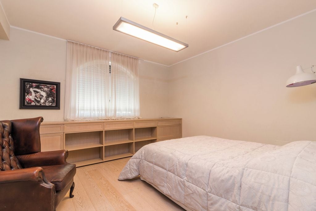Un dormitorio con cama, una silla, un escritorio y una ventana con cortinas.