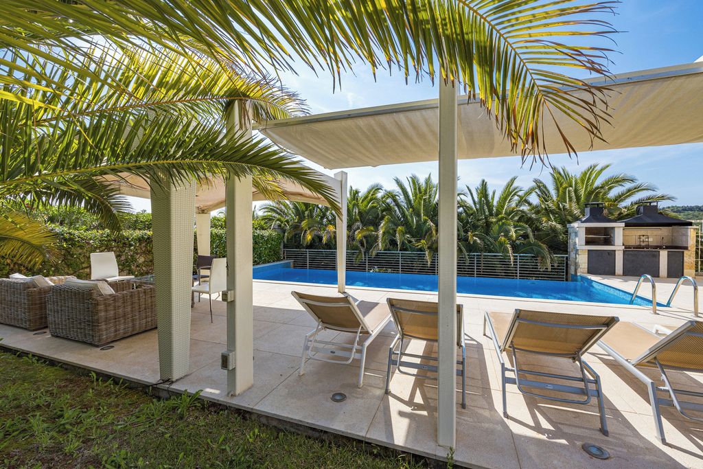 Un espacio exterior techado con piscina, sillas de descanso y una pérgola que da sombra.