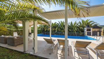 Un espacio exterior techado con piscina, sillas de descanso y una pérgola que da sombra.