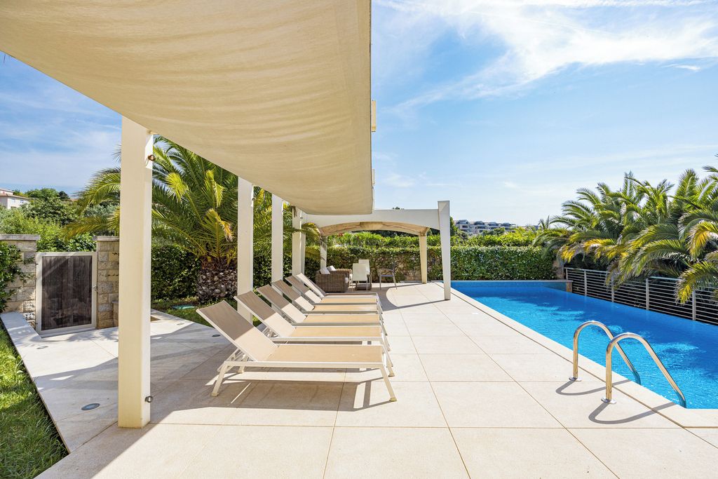 Zona de piscina exterior techada con sillas de descanso y una piscina azul cristalina.