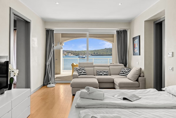 A modern bedroom with a large bed, a sofa, and a view of the sea.