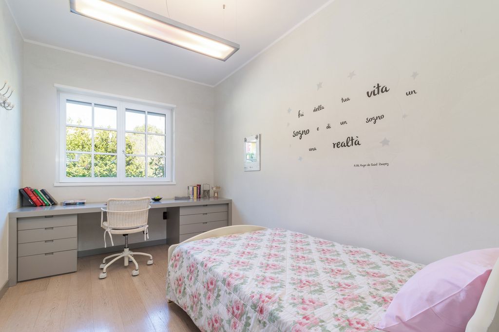 Un dormitorio con cama, escritorio y silla. Se ve una ventana con vista a árboles.