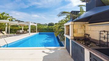 A swimming pool with a patio area, a barbecue grill, and a stone wall.