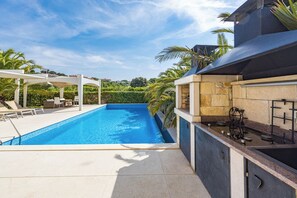 A swimming pool with a patio area, a barbecue grill, and a stone wall.