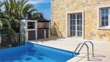 A swimming pool with a stone wall and a grill area.