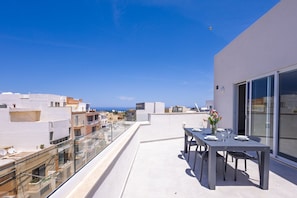 A rooftop terrace with a table set for dining, overlooking a cityscape and the sea. - Spacious Penthouse in the Heart of Gharghur (Hal Gharghur)