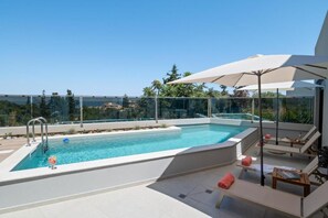 Ein Pool auf dem Dach mit klarem, blauem Wasser, umgeben von Liegestühlen und Sonnenschirmen, mit Blick auf eine Stadtlandschaft.