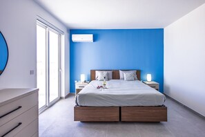 A modern bedroom with a large bed, bedside tables, a nightstand, a dresser, and a wall-mounted air conditioner. - Spacious 4 Bedroom Apartment in Peaceful Gharghur (Hal Gharghur)