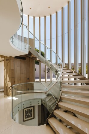 A modern interior with a curved glass staircase leading to a lower level. - Gatsby Mansion - Grand Hollywood Hills Estate with Endless City Vistas (Hollywood Hills, Los Angeles)