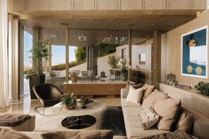 A modern living room with a sofa, armchair, and coffee table, featuring a view of a staircase and outdoor greenery. - Gatsby Mansion - Grand Hollywood Hills Estate with Endless City Vistas (Hollywood Hills, Los Angeles)