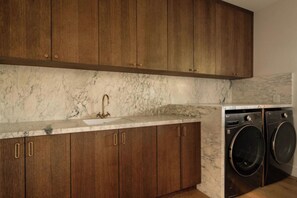 A kitchen with wooden cabinets, a marble countertop, and a washing machine. - Longridge Crest - Gated Studio City Canyon Home (Studio City)