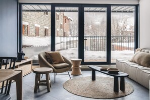 A modern living room with a large sliding glass door leading to a snowy outdoor area. - Les Chalets du Grand Hôtel  (Saint-Chaffrey)