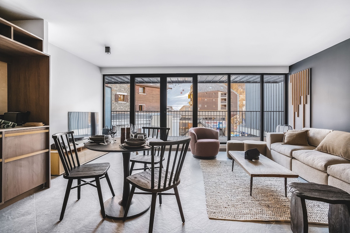 A modern living space with a dining area, a sofa, and a view of the cityscape through large windows.