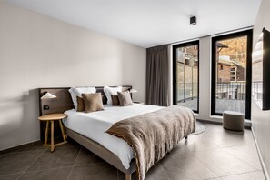 A modern bedroom with a large bed, a small stool, and a view of the outside. - Les Chalets du Grand Hôtel  (Saint-Chaffrey)