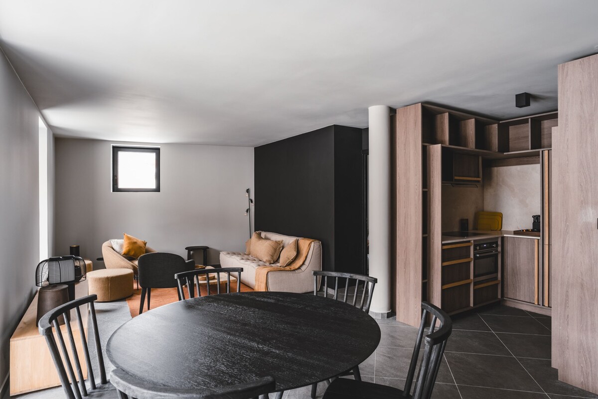 A modern living space with a dining area, a sofa, a coffee table, and a kitchen area.