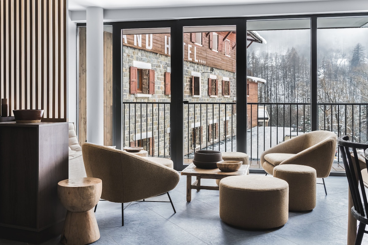 A modern interior with a balcony, wicker furniture, and a view of a building with stone walls.