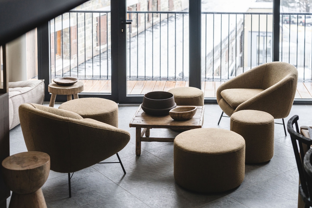 A modern interior with a sofa, armchairs, ottomans, and a small table with bowls.