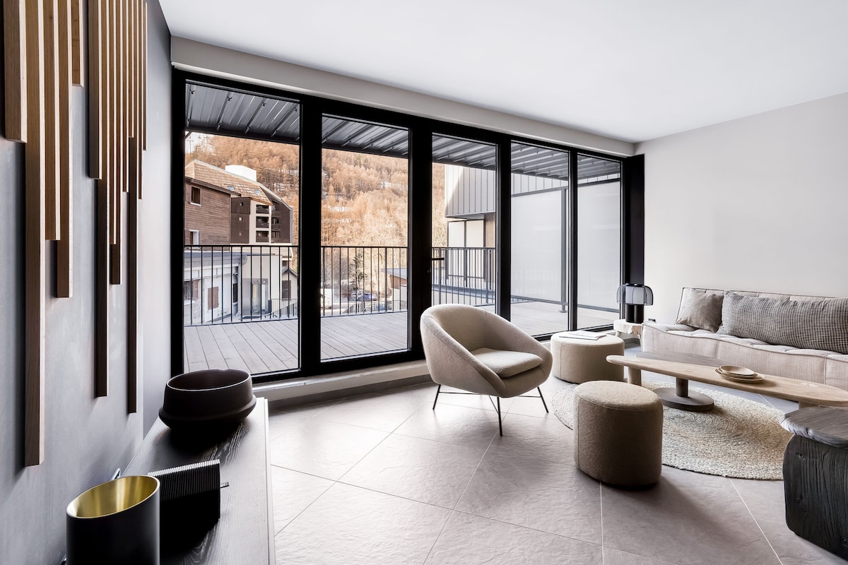 A modern living room with a large sliding glass door, a sofa, a chair, a coffee table, and a small side table.