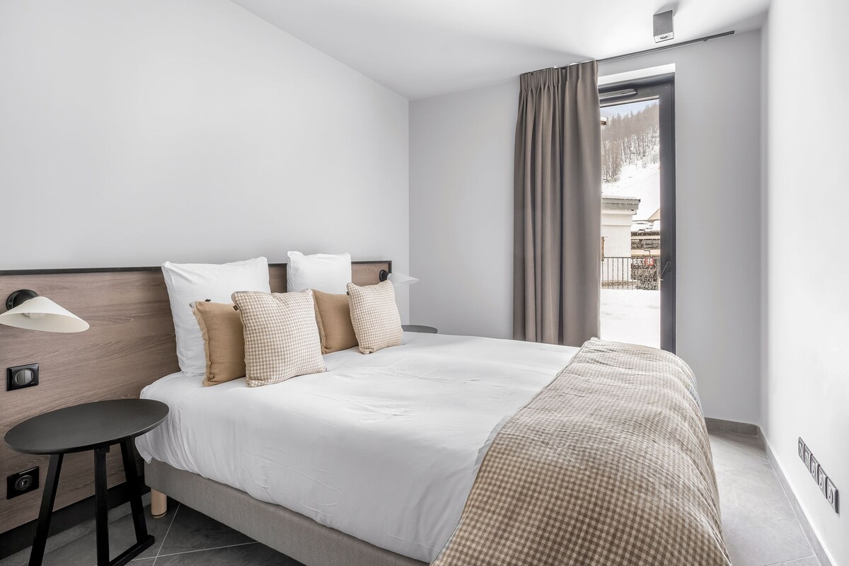 A hotel room with a bed, bedside table, lamp, and a view of a snowy landscape through the window.