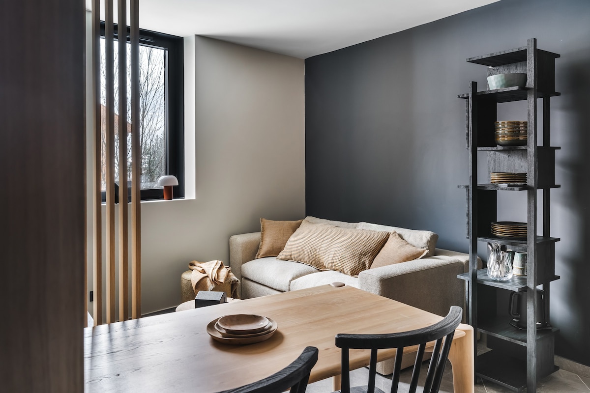 A modern interior with a dining table, chairs, a sofa, and a shelving unit.