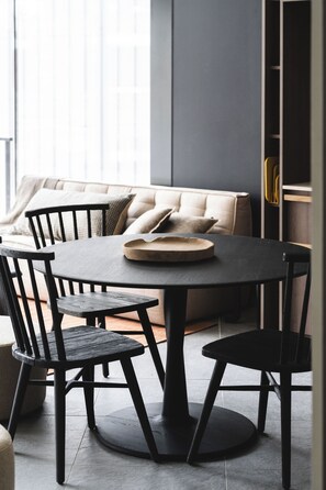 Een moderne eethoek met een ronde tafel en vier stoelen, een bank met kussens, en een boekenkast op de achtergrond.