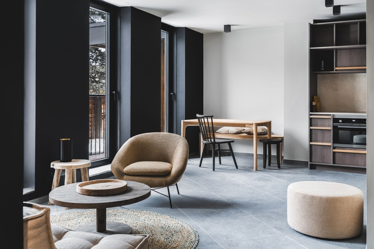 A modern interior with a round table, a chair, a sofa, and a kitchen area.