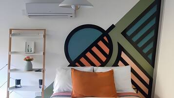 Un dormitorio con cama, aire acondicionado de pared, repisa con adornos y una gran obra de arte abstracta en la pared.