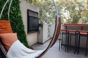 Un sillón colgante con cojines, un televisor de pared y una zona de bar con taburetes.