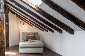 A loft bedroom with exposed wooden beams, a light fixture, and a sofa with a magazine. - Stay in Historic Madrid Centre (Madrid)