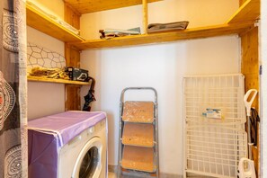 Ein Waschraum mit Waschmaschine, Wäscheständer und Regalen mit gefalteter Kleidung und Reinigungsmitteln.