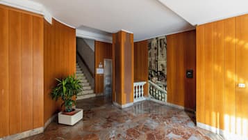 Un hall d’entrée avec des boiseries, un sol en marbre, un escalier et un tableau au mur.