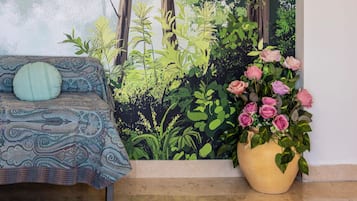 Une pièce avec un canapé à motifs, une grande fenêtre et une plante en pot ornée de fleurs roses.