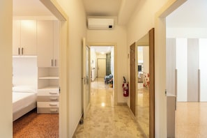 A hotel hallway with a bed, a wardrobe, a fire extinguisher, and a bathroom visible in the distance. - HouSmart Giambologna 8 (Bologna)