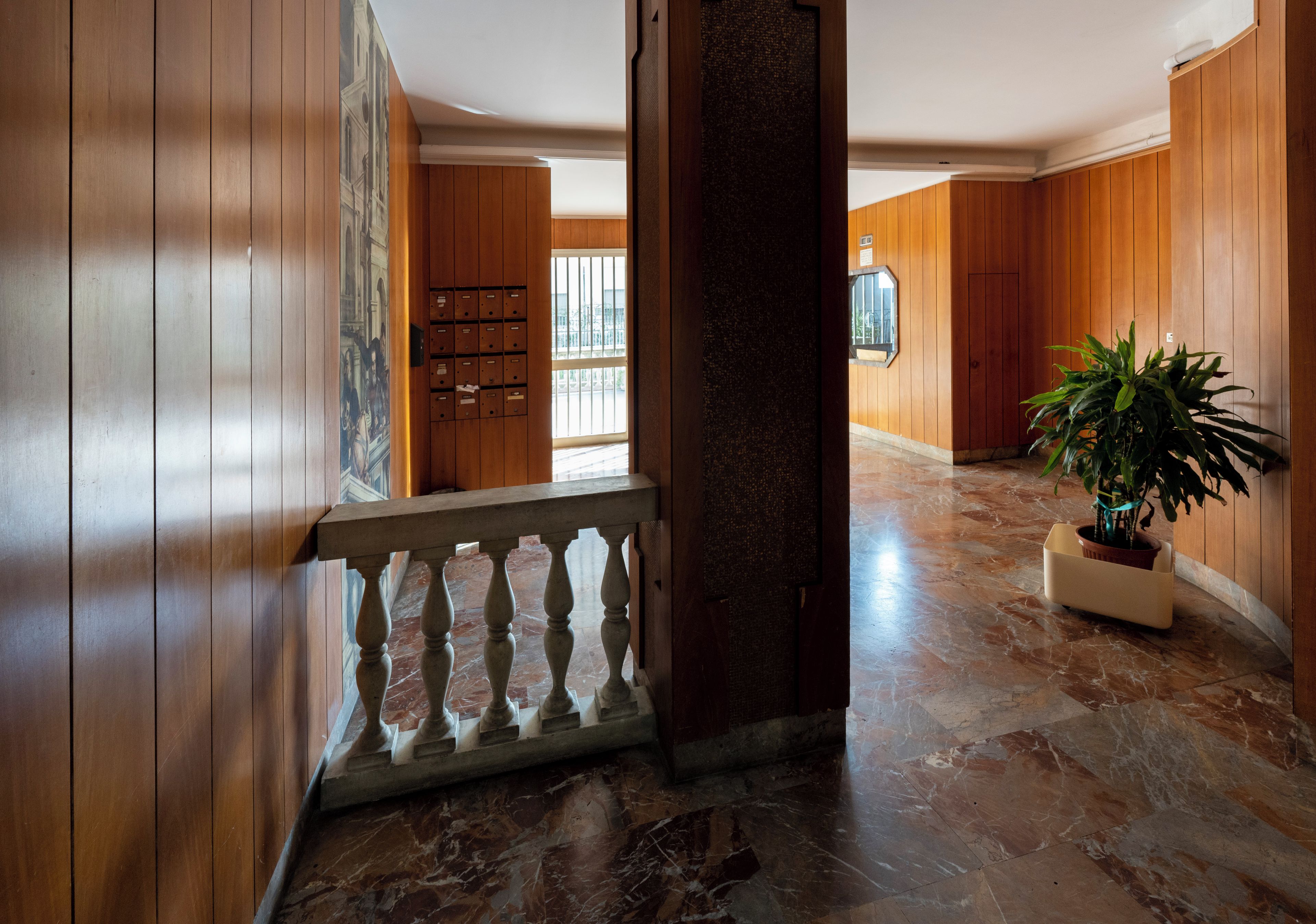 Un pasillo con paneles de madera, piso de mármol y una planta en maceta.