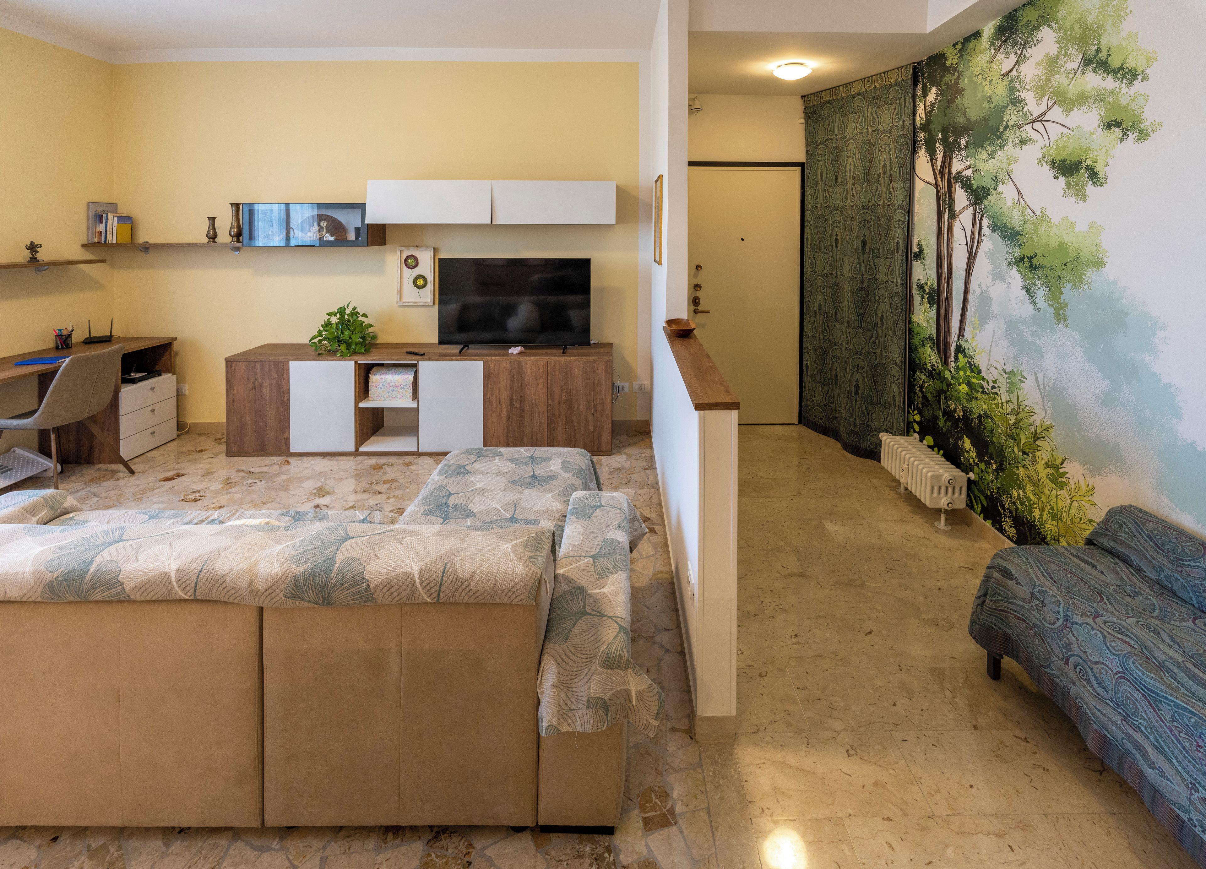 Espai vital compacte amb sofà, televisió, escriptori i un mural.