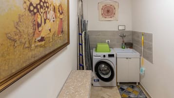 Une petite buanderie comprenant un lave-linge, un étendoir et un petit évier.